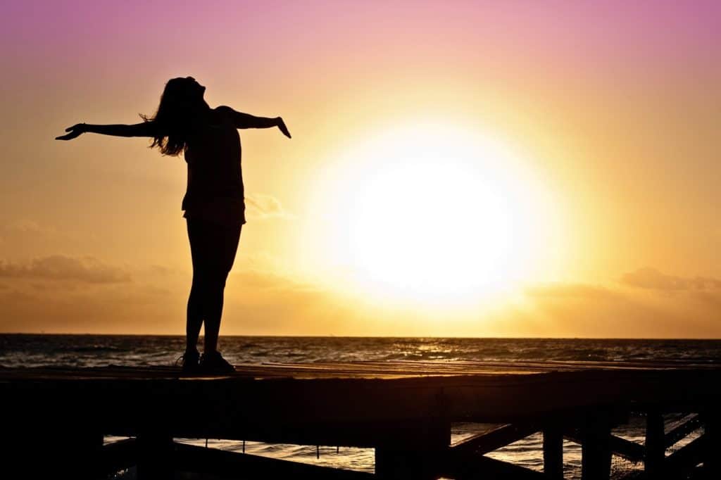 Women with arms outstretched on beach at sunrise